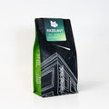 Green and black coffee bag with 'Hazelnut' flavor label on a white background