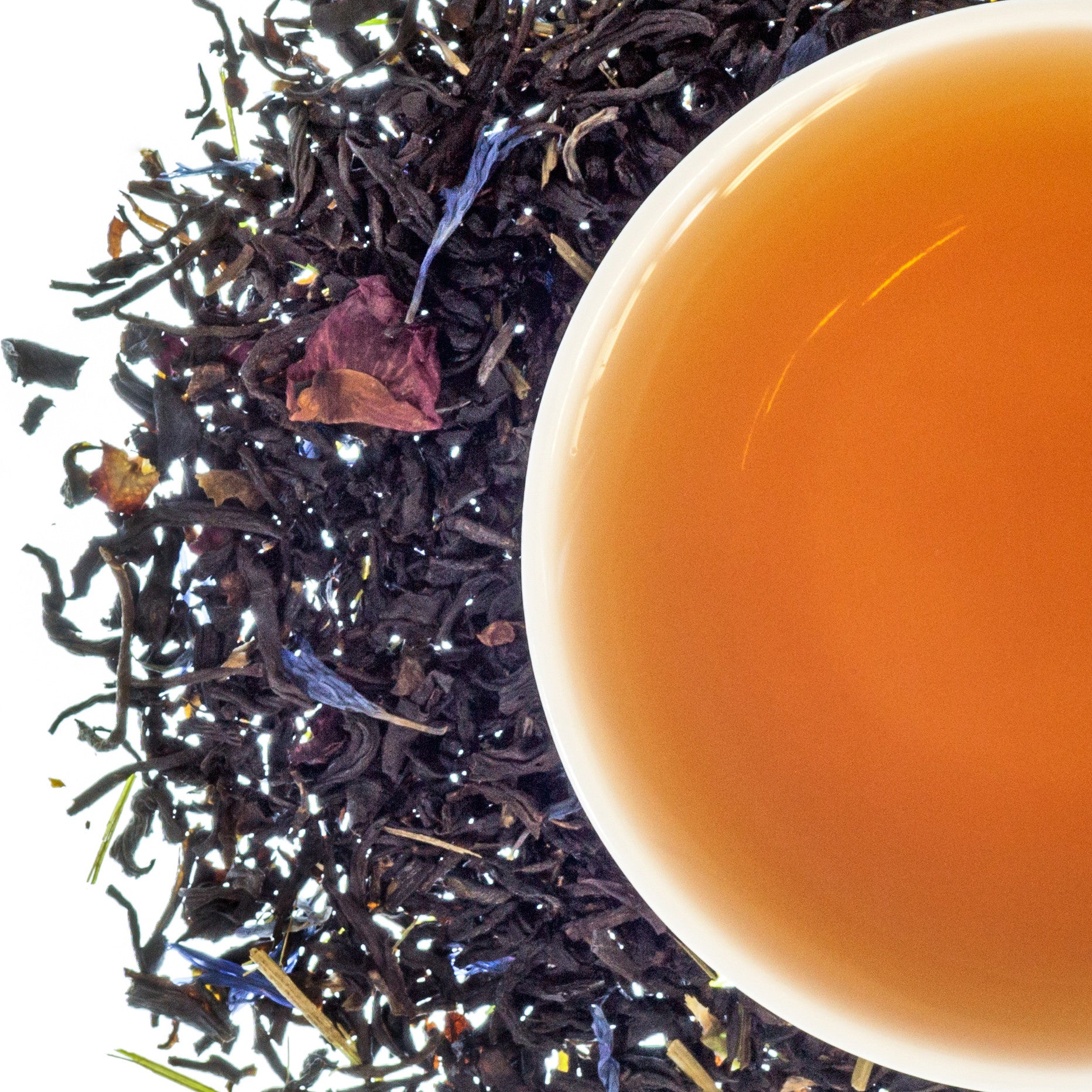 A top down image of a cup of tea with dried loose leaf tea around it on a white background.