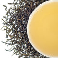 A top-down image of a cup of green tea with visible tea leaves scattered around.