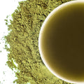 A close-up image of matcha powder with a cup of tea made from the powder in the background.
