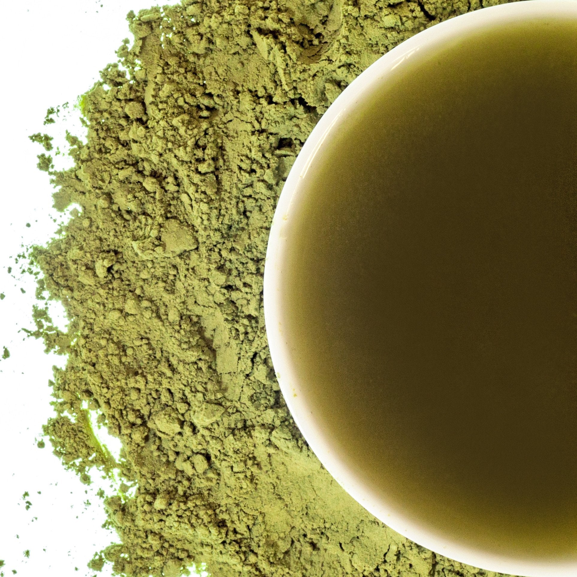 A close-up image of matcha powder with a cup of tea made from the powder in the background.