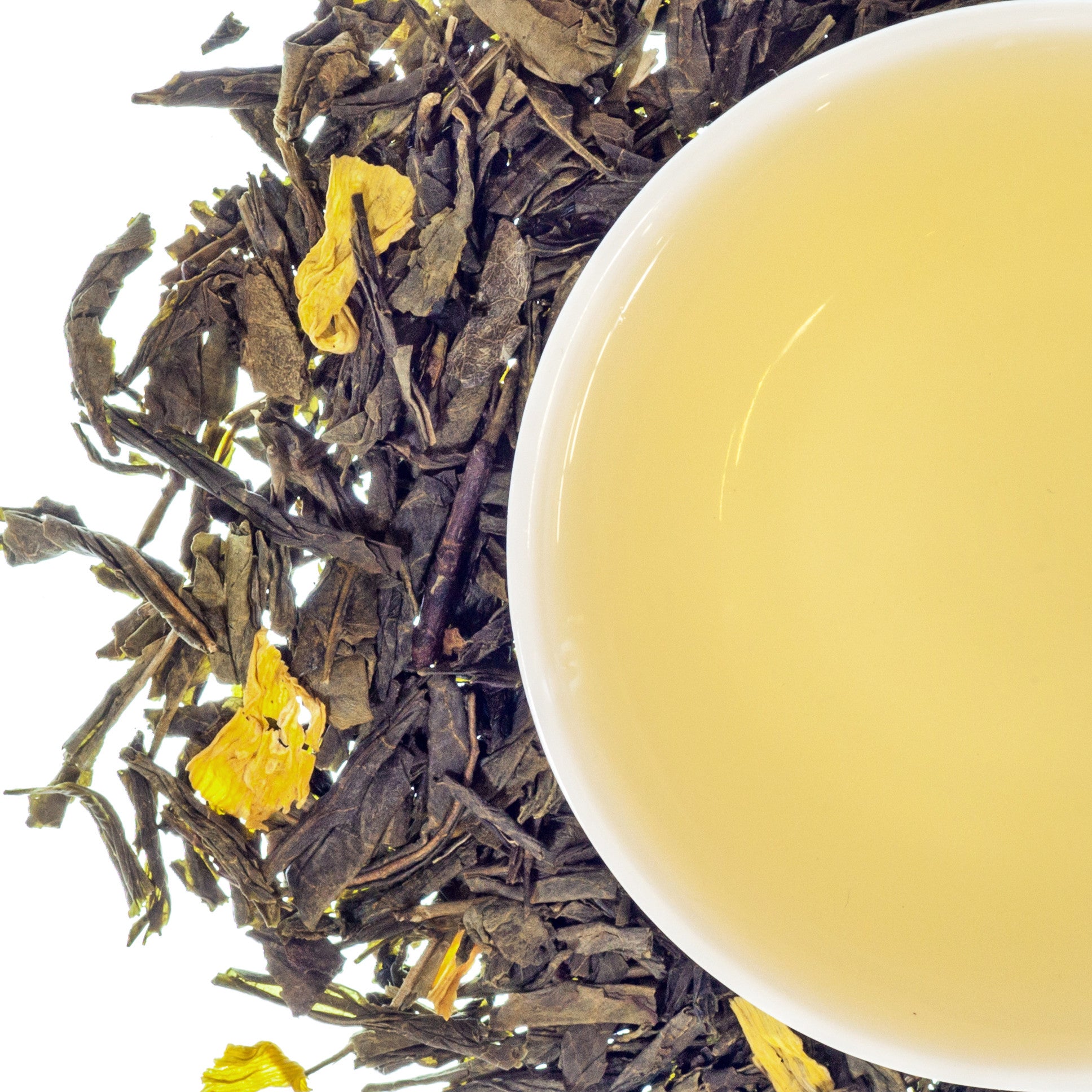 A cup of green tea with mango next to a pile of dried mango leaves and tea leaves on a white background.