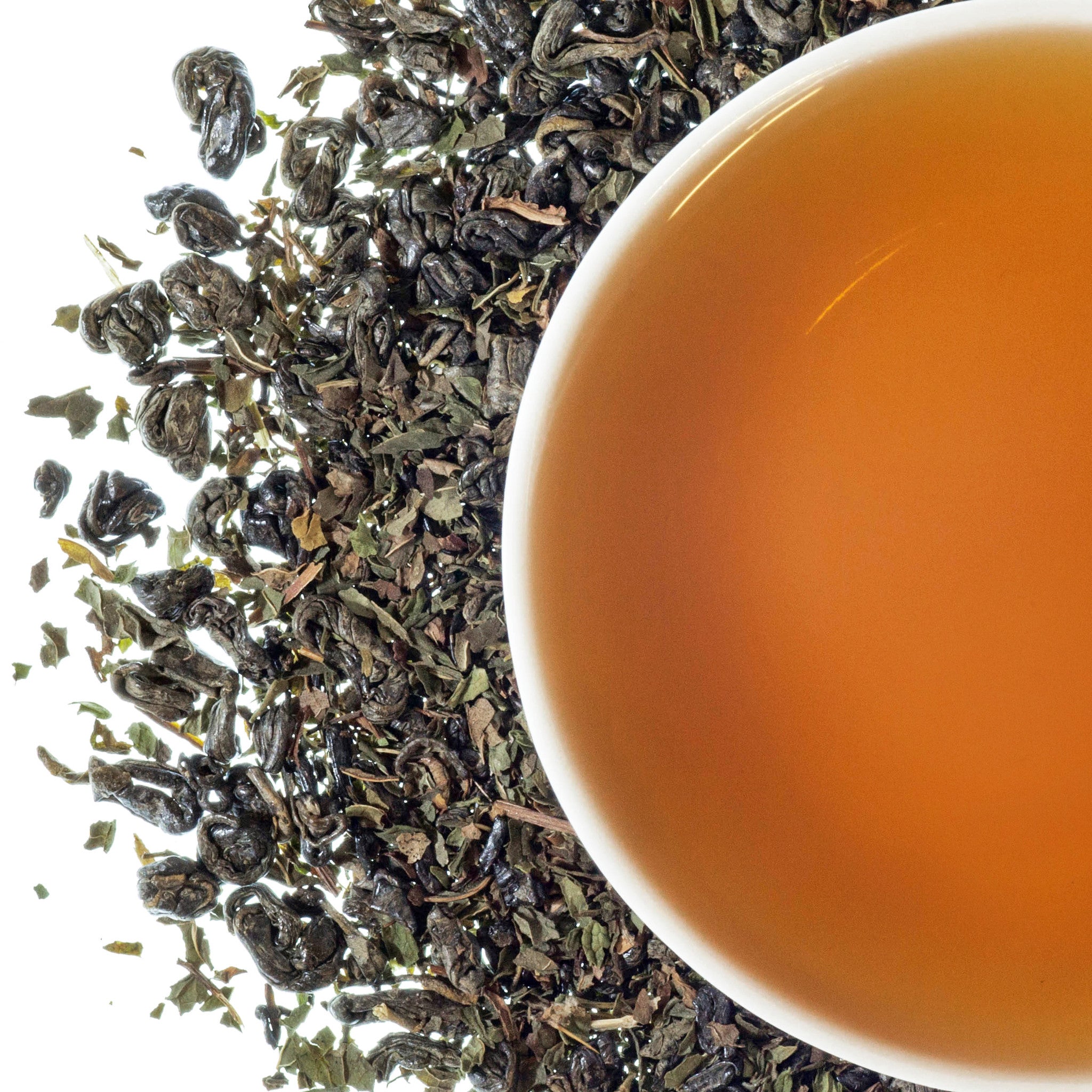 A cup of tea with mint leaves scattered around, indicating the tea is a mint tea blend.