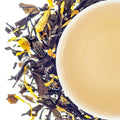 A top-down image of a white tea bag with loose tea leaves scattered around, presenting a peach-like aroma.