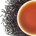 A top down image of a cup of tea with dried loose leaf around it on a white background