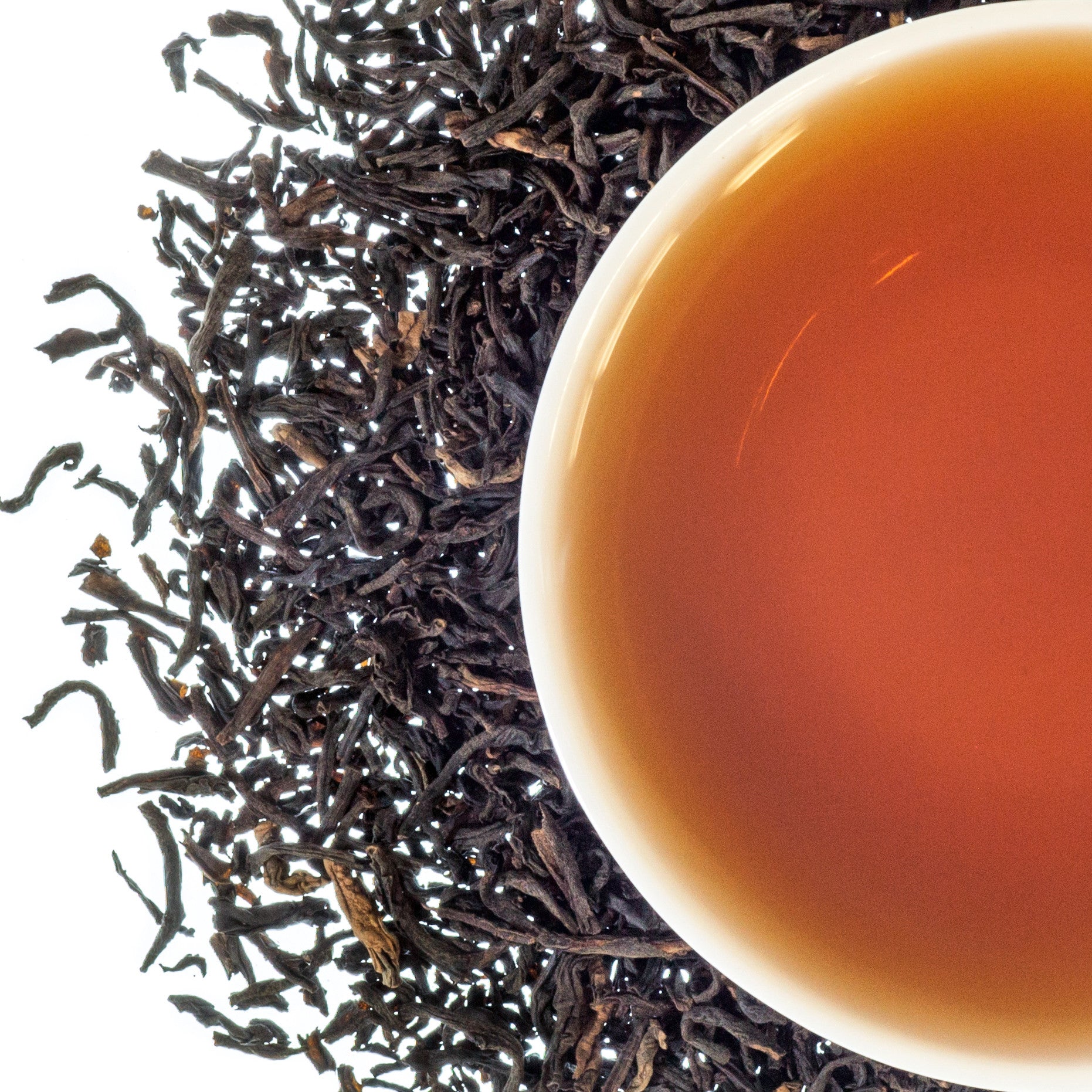 A top down image of a cup of tea with dried loose leaf around it on a white background