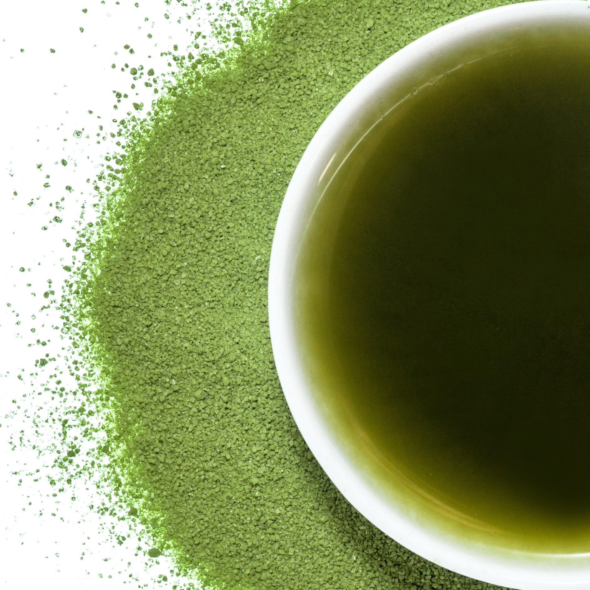 A bowl of matcha with matcha powder around it on a white background