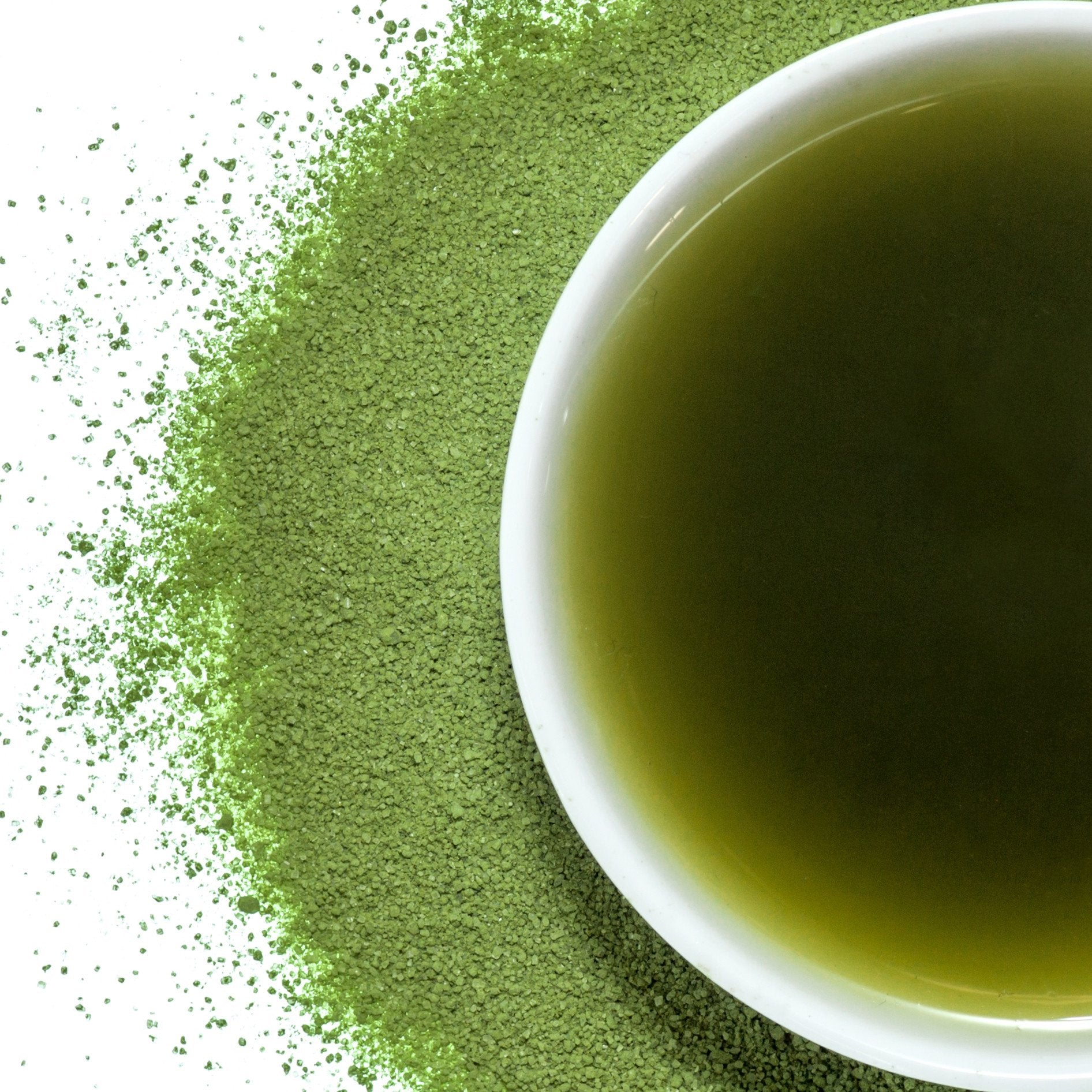A bowl of matcha with matcha powder around it on a white background